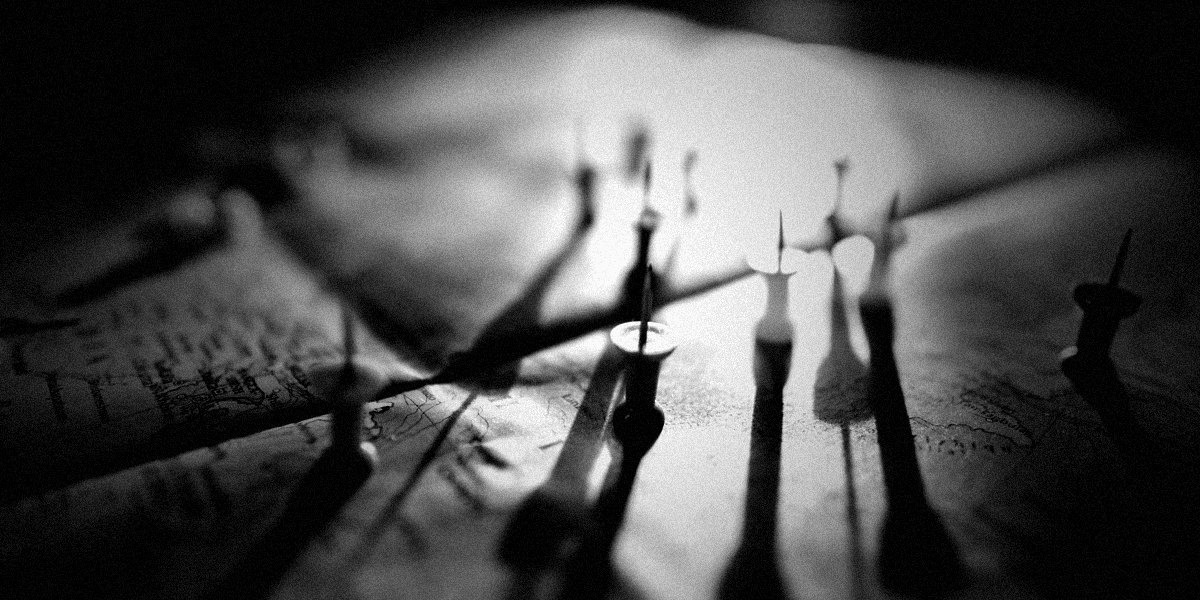 Desaturated, grainy close-up of colored pushpins on a map with dramatic backlight and long shadows