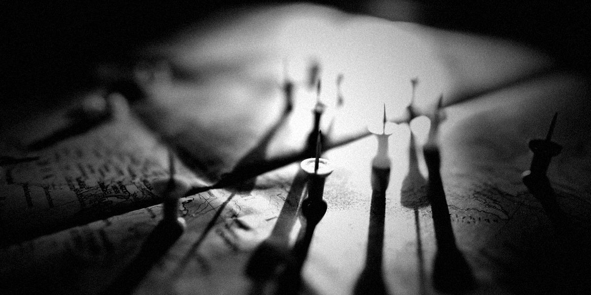 Desaturated, grainy close-up of colored pushpins on a map with dramatic backlight and long shadows